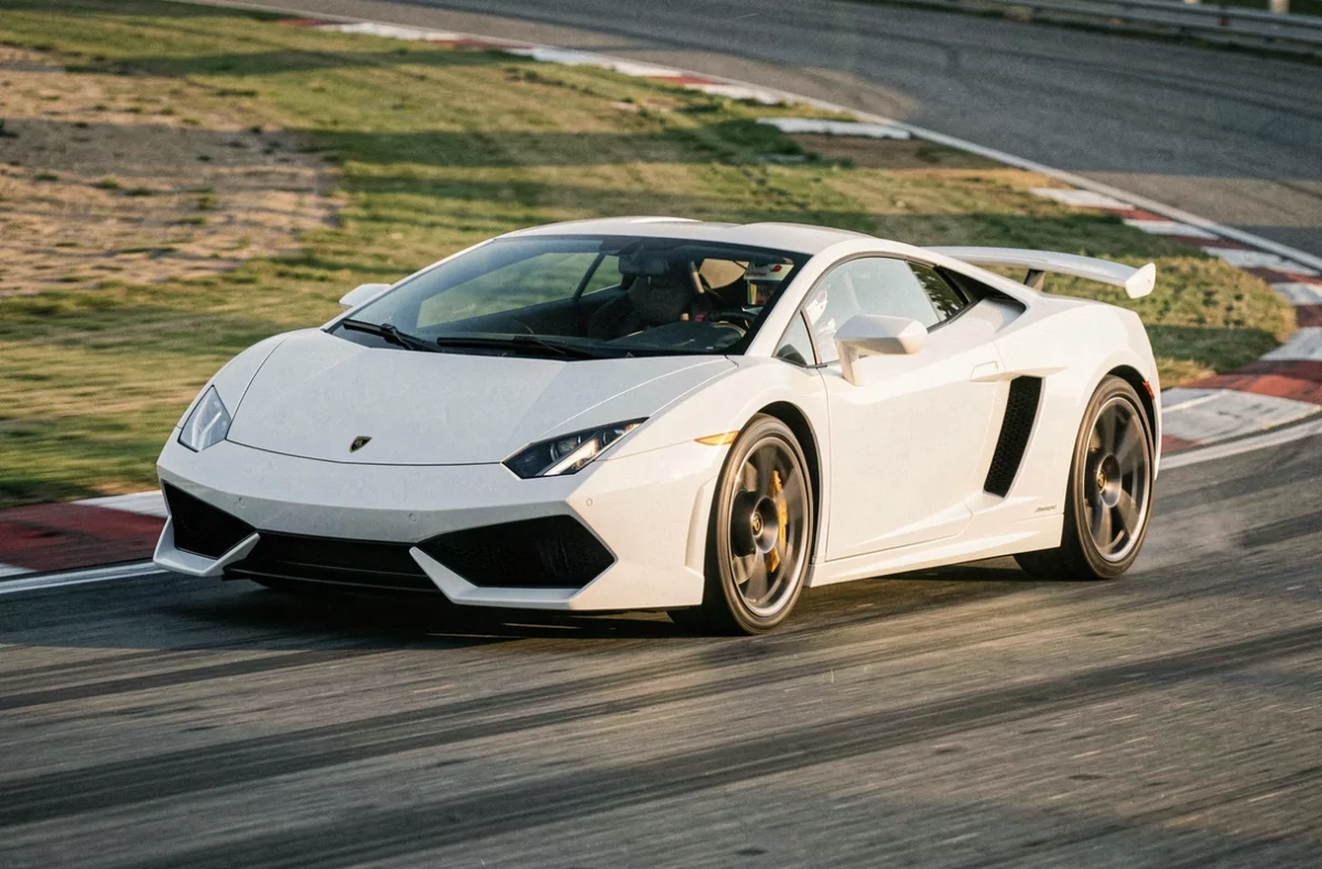 Lamborghini Gallardo blanche en pleine accélération dans un virage de circuit, pilote en tenue de course avec casque intégral