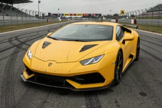 Lamborghini Huracán jaune garée à l'entrée d'un circuit de course, vue 3/4 avant en contre-plongée mettant en valeur la carrosserie sportive
