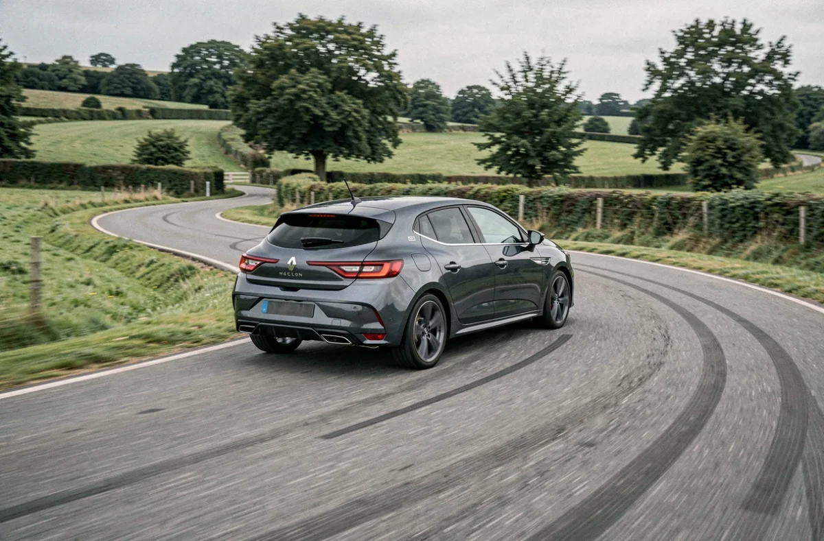Renault Megane grise en train de prendre un virage sur une route de campagne, illustrant sa tenue de route et la stabilité liée à ses dimensions