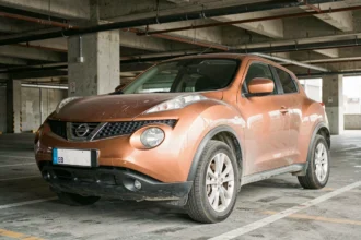 Nissan Juke d'une ancienne année de production présentant des signes d'usure visibles dans un parking urbain